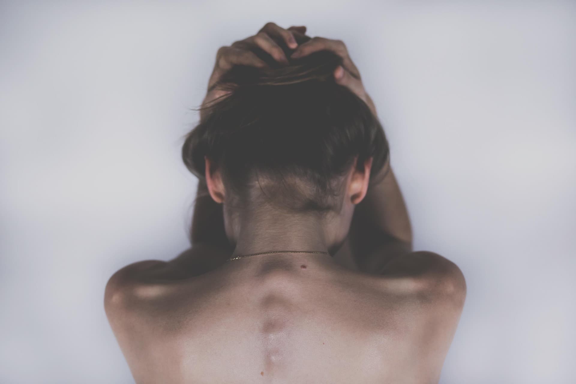 Mujer de espaldas, con los hombros desnudos, sujetándose el cabello con ambas manos